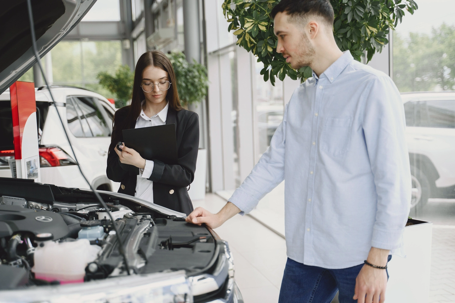 Stern Wagen GmbH - Fahrzeug Einkauf - Ein Autoberater erklärt einem Kunden in einem Autohaus die Details des Motors.